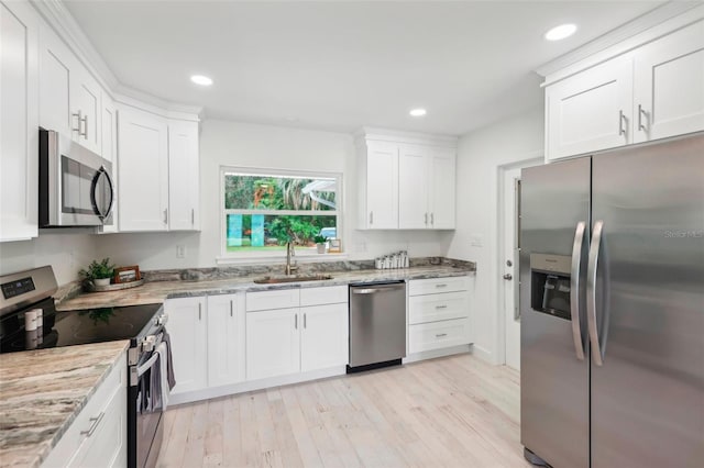 kitchen with stainless steel appliances, sink, light stone countertops, white cabinets, and light hardwood / wood-style floors