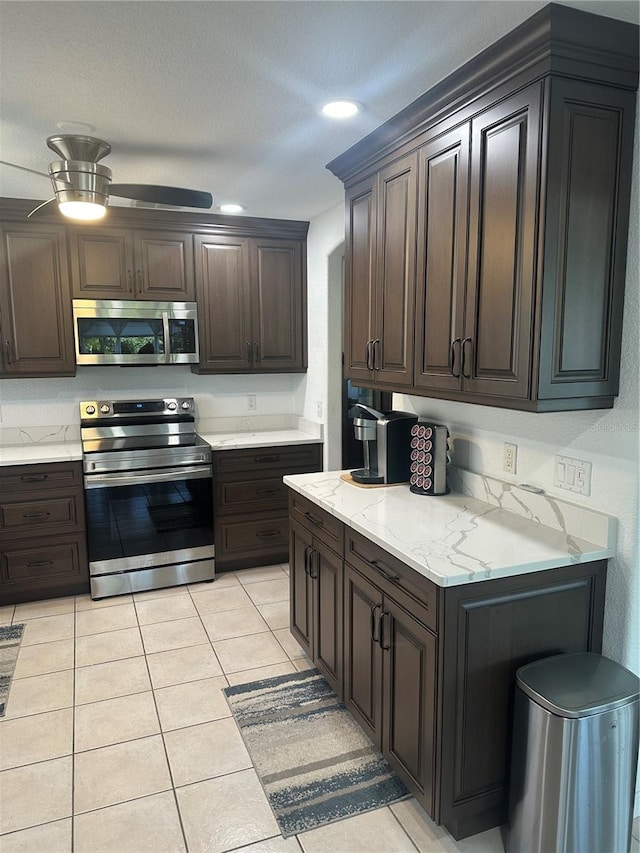 kitchen featuring dark brown cabinetry, ceiling fan, stainless steel appliances, light stone counters, and light tile patterned floors