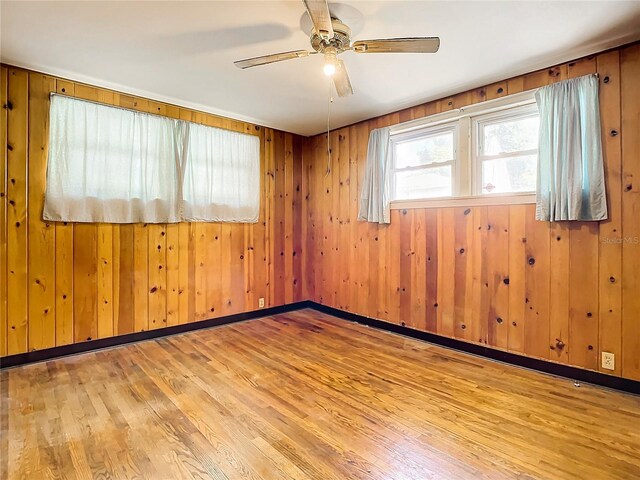 unfurnished room featuring ceiling fan, light hardwood / wood-style flooring, and wood walls