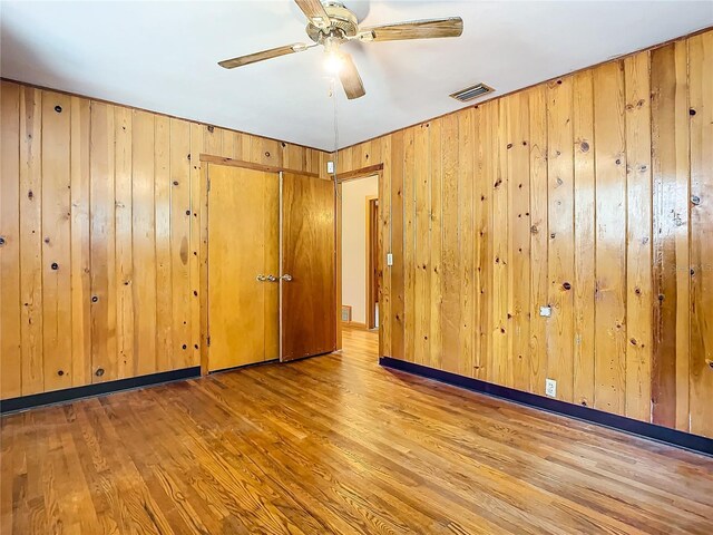 empty room with wooden walls, ceiling fan, and light hardwood / wood-style flooring