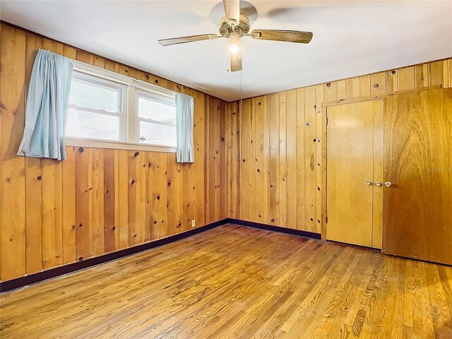 spare room featuring light hardwood / wood-style flooring, wooden walls, and ceiling fan