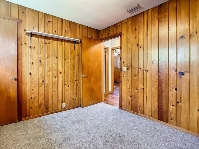 unfurnished bedroom featuring light carpet and wood walls