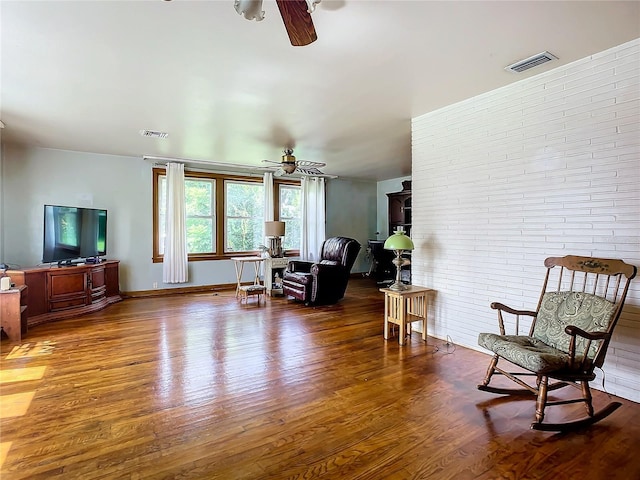 living area featuring hardwood / wood-style flooring, brick wall, and ceiling fan