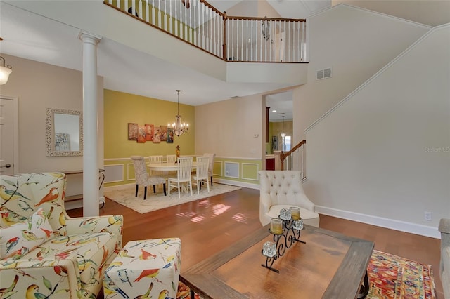 living room featuring decorative columns, a towering ceiling, hardwood / wood-style floors, and a chandelier