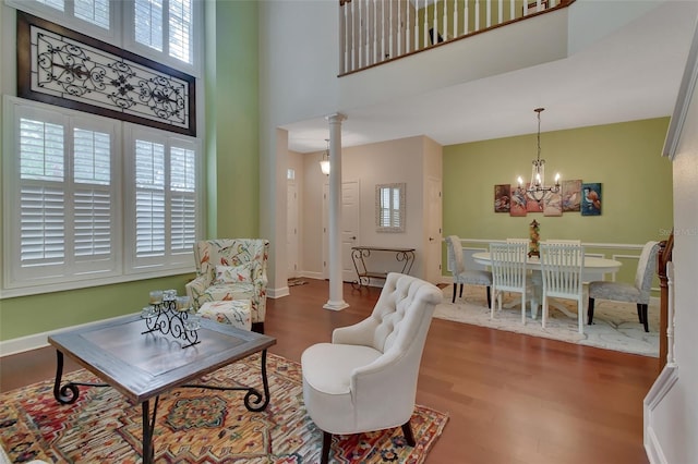 living room featuring plenty of natural light, hardwood / wood-style floors, ornate columns, and an inviting chandelier