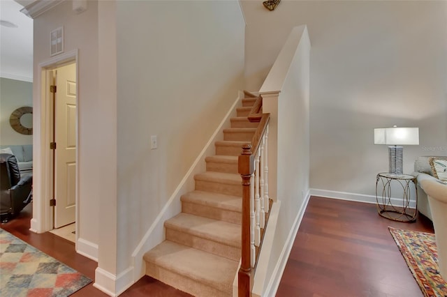 staircase with ornamental molding and dark hardwood / wood-style floors