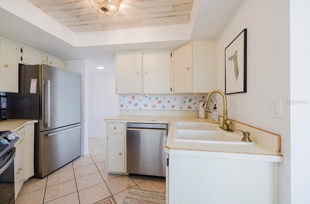 kitchen with appliances with stainless steel finishes, sink, white cabinets, light tile patterned floors, and a tray ceiling