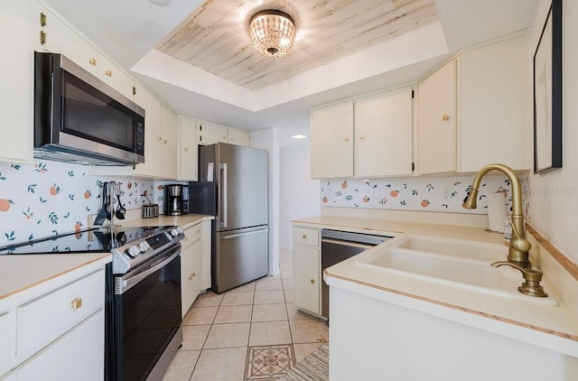 kitchen with light tile patterned floors, appliances with stainless steel finishes, white cabinetry, decorative backsplash, and a raised ceiling