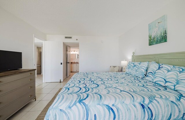 tiled bedroom with a textured ceiling and connected bathroom