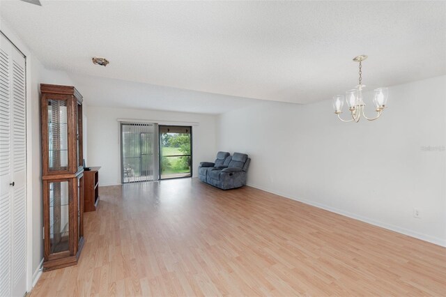 unfurnished living room with a textured ceiling, a chandelier, and light hardwood / wood-style floors