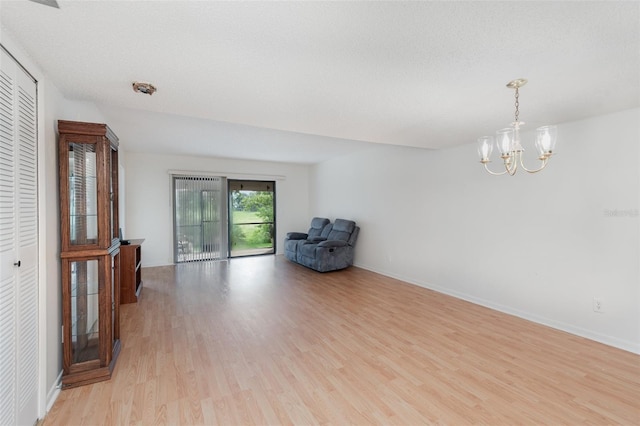 unfurnished room with an inviting chandelier, a textured ceiling, and light wood-type flooring