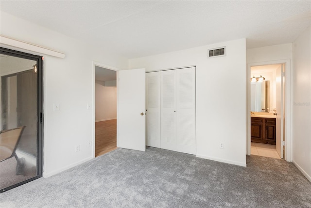 unfurnished bedroom with ensuite bath, light colored carpet, and a closet