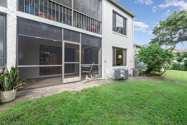 rear view of house featuring a sunroom, cooling unit, and a lawn