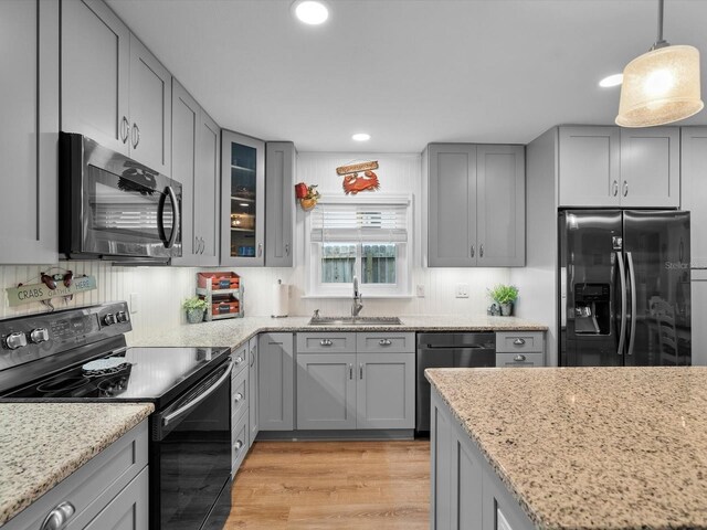 kitchen featuring light wood-type flooring, gray cabinetry, a sink, and black appliances