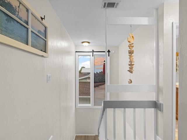 hallway featuring a textured wall, a barn door, an upstairs landing, and visible vents