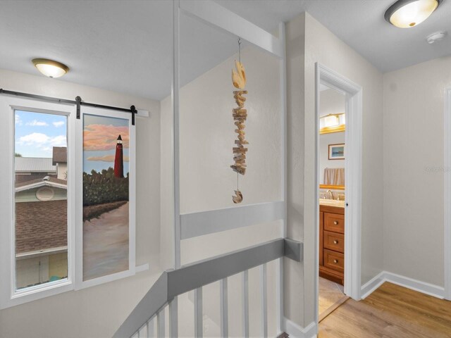 corridor featuring light wood finished floors, a barn door, baseboards, and an upstairs landing