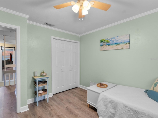 bedroom featuring wood finished floors, visible vents, baseboards, a closet, and crown molding