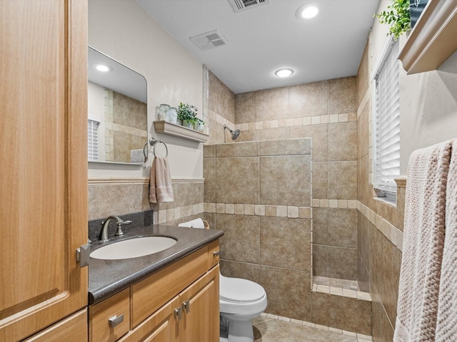 bathroom with a walk in shower, toilet, vanity, visible vents, and tile walls