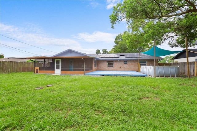 back of house featuring a lawn, a sunroom, and solar panels