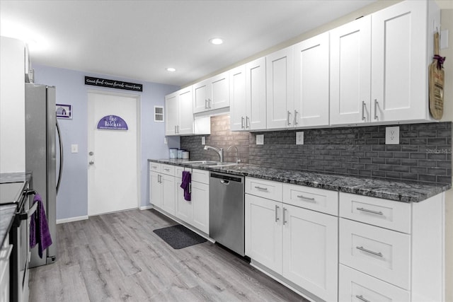 kitchen with stainless steel appliances, white cabinets, a sink, light wood-type flooring, and dark stone counters