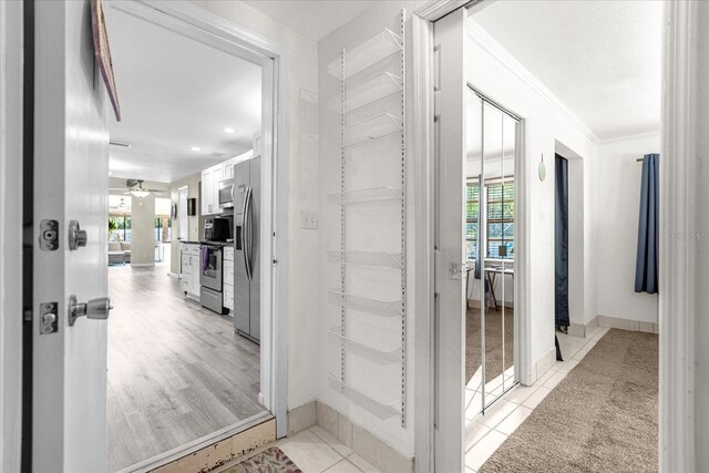 corridor featuring light wood-type flooring, ornamental molding, and plenty of natural light