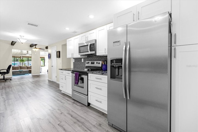 kitchen with stainless steel appliances, visible vents, light wood-style floors, white cabinets, and decorative backsplash