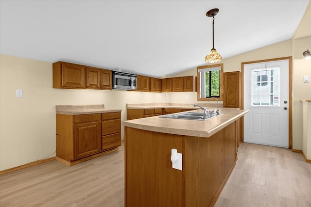 kitchen with brown cabinets, decorative light fixtures, light countertops, stainless steel microwave, and an island with sink