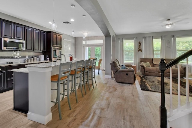 kitchen with appliances with stainless steel finishes, a breakfast bar area, light wood-type flooring, and a kitchen island with sink