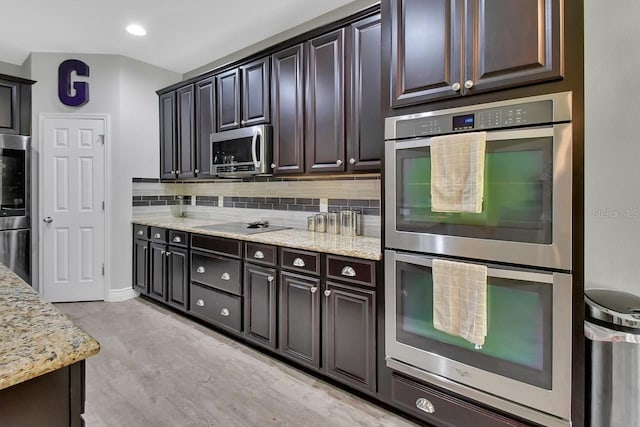 kitchen with light stone counters, appliances with stainless steel finishes, dark brown cabinetry, backsplash, and light wood-type flooring