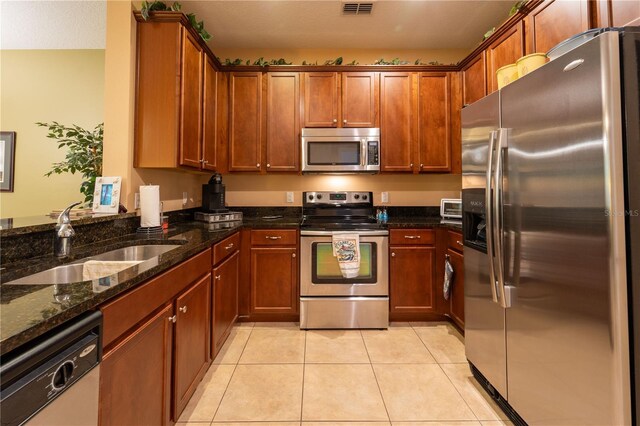 kitchen with light tile patterned flooring, appliances with stainless steel finishes, sink, and dark stone countertops