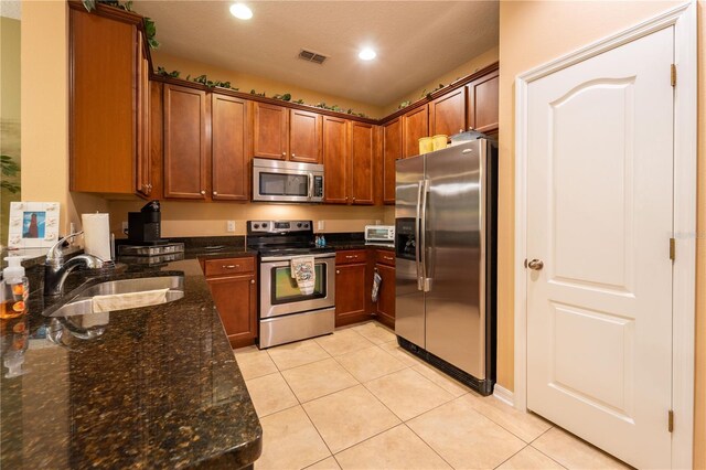 kitchen featuring sink, stainless steel appliances, light tile patterned flooring, and dark stone counters