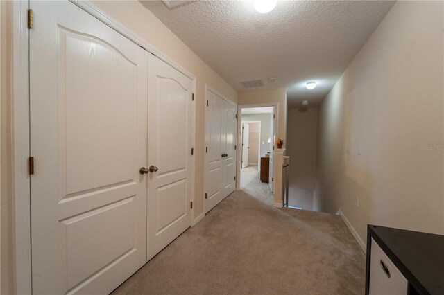 hall with a textured ceiling and light carpet