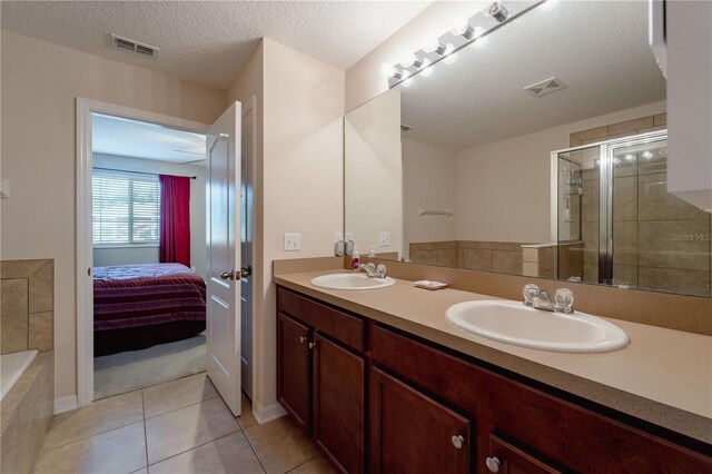 bathroom featuring plus walk in shower, dual bowl vanity, tile patterned flooring, and a textured ceiling