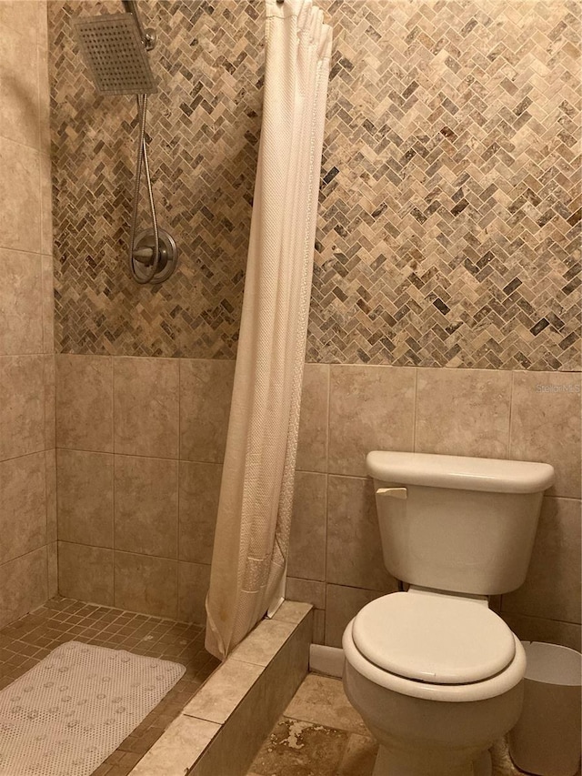 bathroom featuring tile walls, curtained shower, and toilet