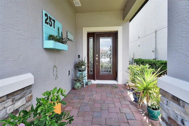 entrance to property featuring visible vents and stucco siding