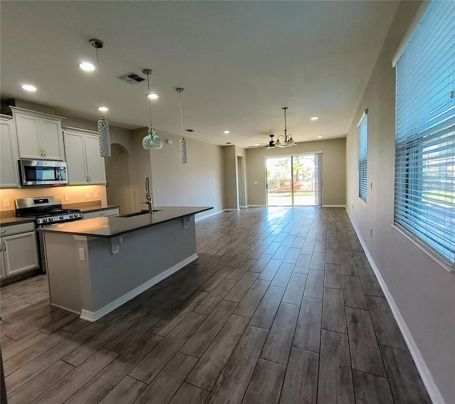 kitchen featuring sink, appliances with stainless steel finishes, hanging light fixtures, an island with sink, and white cabinets