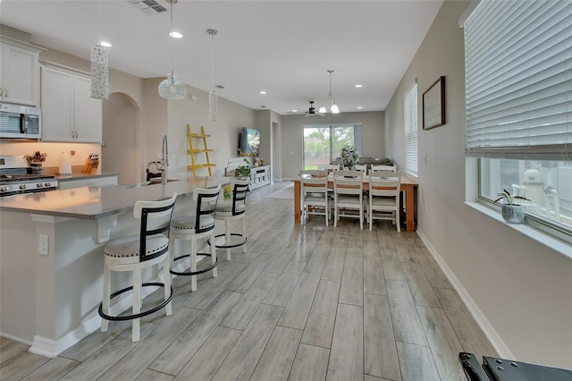 kitchen with white cabinetry, hanging light fixtures, stainless steel appliances, a kitchen bar, and a large island with sink