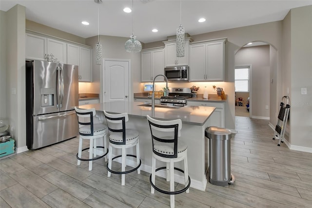 kitchen featuring white cabinetry, decorative light fixtures, stainless steel appliances, and a center island with sink