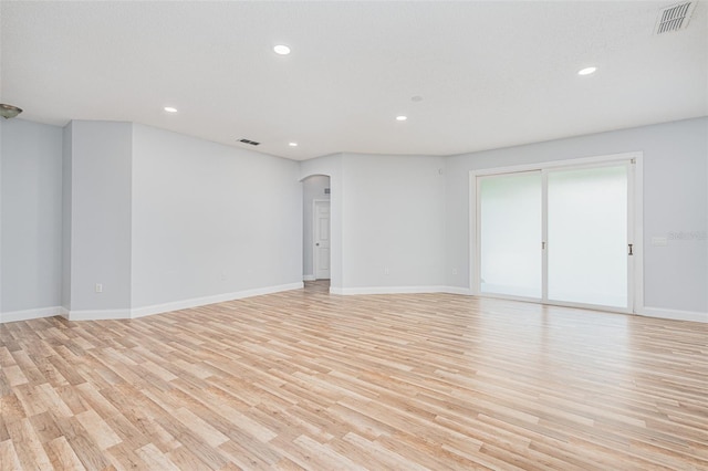 empty room with light wood-type flooring, visible vents, arched walkways, and recessed lighting