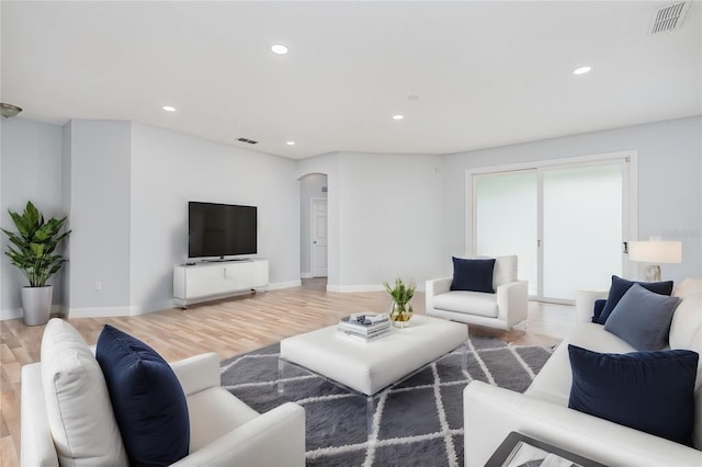 living area with visible vents, arched walkways, and light wood-style flooring