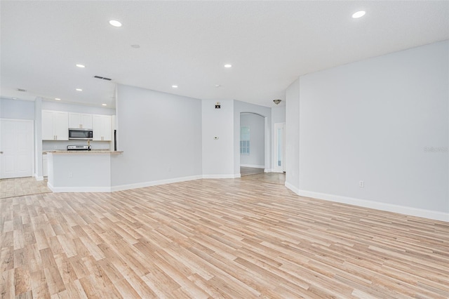 unfurnished living room with arched walkways, recessed lighting, visible vents, baseboards, and light wood finished floors