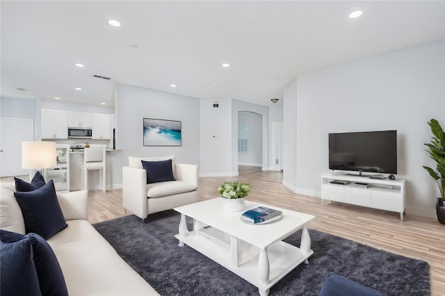 living area featuring arched walkways, visible vents, light wood-style flooring, and recessed lighting