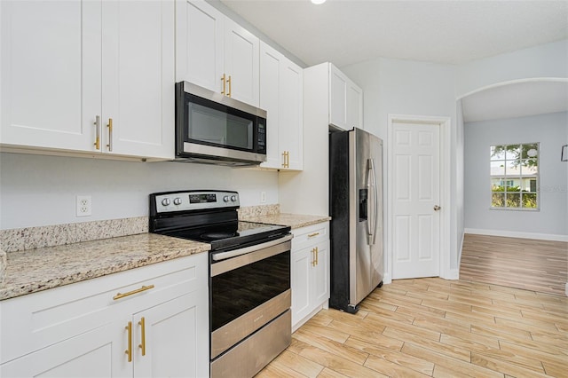 kitchen with arched walkways, white cabinetry, appliances with stainless steel finishes, light stone countertops, and light wood finished floors