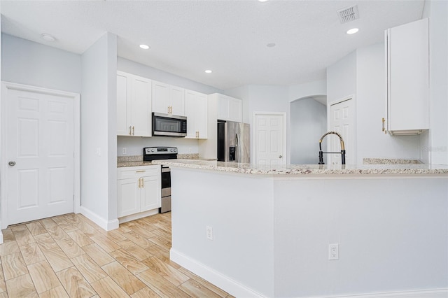 kitchen featuring visible vents, a peninsula, light stone countertops, stainless steel appliances, and white cabinetry