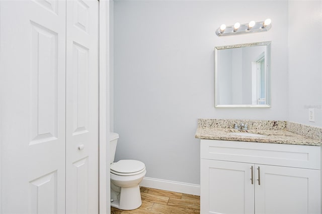 bathroom with a closet, toilet, vanity, wood finished floors, and baseboards