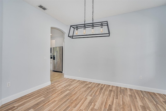 unfurnished dining area featuring light wood-type flooring, arched walkways, visible vents, and baseboards