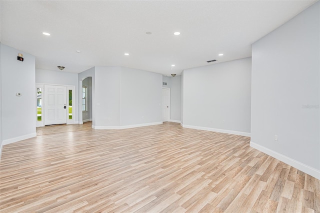 empty room with light wood finished floors, baseboards, arched walkways, and recessed lighting