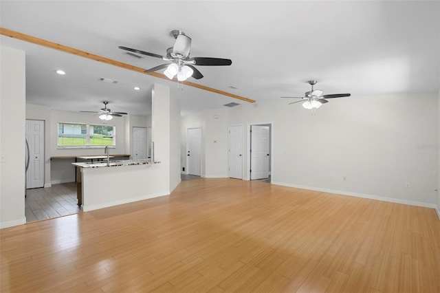 unfurnished living room with lofted ceiling, light hardwood / wood-style floors, sink, and ceiling fan