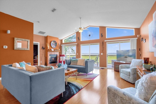 living room featuring light hardwood / wood-style flooring, ceiling fan, high vaulted ceiling, and a fireplace