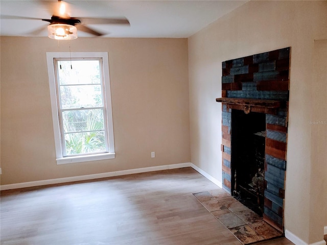 unfurnished living room featuring a wealth of natural light, ceiling fan, light hardwood / wood-style flooring, and a brick fireplace